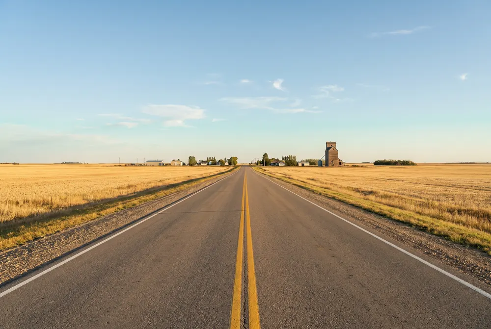 Prairie highway toward a town with a grain elevator